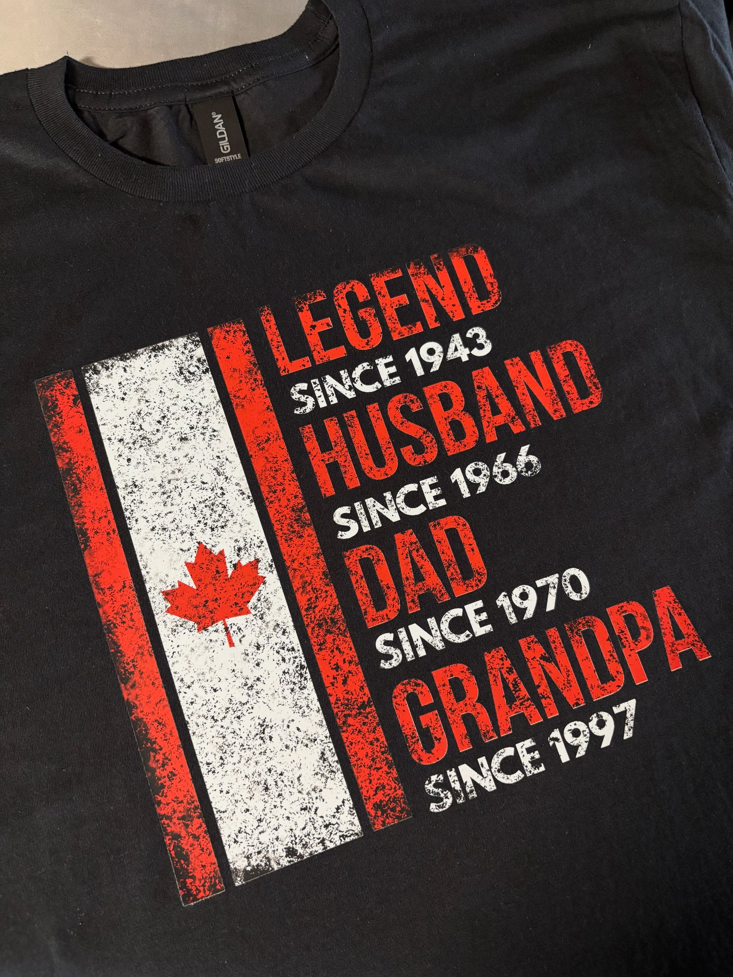 Black t-shirt with red and white text and a maple leaf design on a beige background